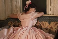 a woman sitting on top of a couch wearing a pink dress and flower in her hair