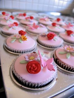 cupcakes with pink frosting decorated with flowers and butterflies are on a baking sheet