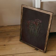 an old photo frame sitting on the floor next to a window with flowers in it