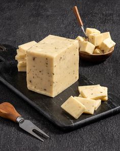 some kind of cheese on a black plate with a wooden spoon and knife next to it