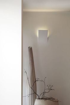 a white vase sitting on top of a wooden table next to a wall mounted light