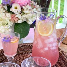 a pitcher and two glasses sitting on a wicker table with flowers in the background