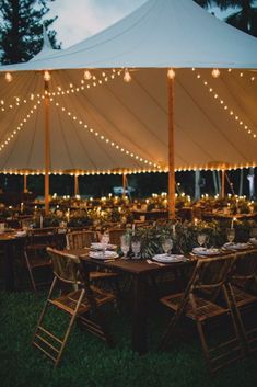 an outdoor tent with tables and chairs set up for dinner under string lights at night