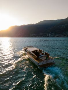 a small boat is traveling on the water near some hills and mountains in the distance