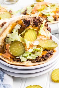 two tacos filled with meat, lettuce and pickles on top of a white plate