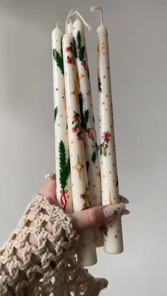 a woman's hand holding four white candles with holly decorations on them, all wrapped in twine