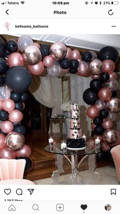 a table topped with a cake covered in black, pink and silver balloons next to a mirror