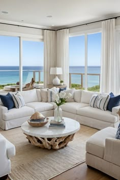 a living room filled with white furniture and large windows overlooking the ocean on a sunny day