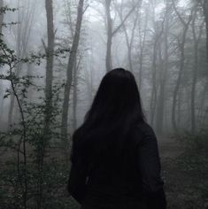 a woman standing in the middle of a forest on a foggy day with her back to the camera