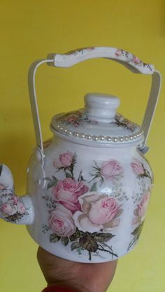 a hand holding a white tea kettle with pink roses painted on the front and sides