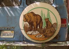 a bear and cub sticker on the back of a blue car with trees in the background