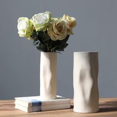 two white vases with flowers in them sitting on a table next to each other