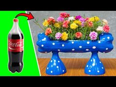 a blue vase filled with flowers next to a coca cola bottle on top of a table