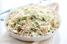 a white bowl filled with coleslaw on top of a striped napkin next to a spoon