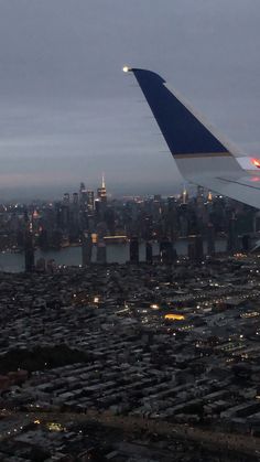 an airplane wing flying over a large city at night with the lights on and buildings lit up in the background