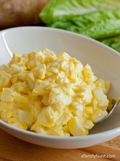 a white bowl filled with scrambled eggs on top of a wooden table next to lettuce