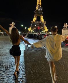 two people walking in front of the eiffel tower at night with their arms outstretched