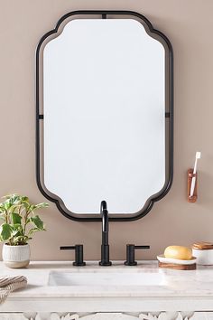 a bathroom mirror sitting on top of a white counter next to a potted plant