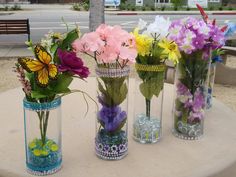 four vases filled with colorful flowers sitting on top of a white table next to a bench