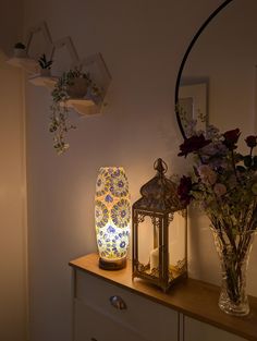 two vases with flowers are sitting on a dresser next to a lantern and flower arrangement