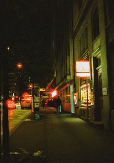 a city street at night with cars parked on the side walk and people walking down the sidewalk