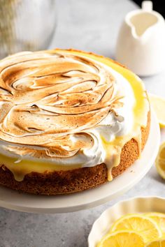 a lemon meringue cheesecake on a white plate next to sliced lemons