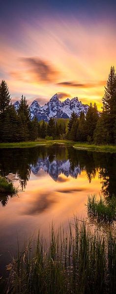 the sun is setting over a lake with mountains in the background and trees around it