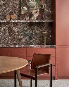 two chairs sitting next to each other near a wooden table and red wall with artwork on it