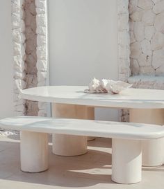 a white table and two benches in front of a stone wall with shells on it