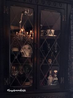 a black china cabinet with candles and dishes on it's glass doors, in a dark room