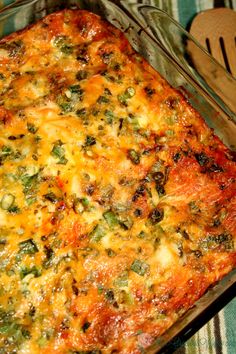 a casserole with cheese and vegetables in a glass dish next to a wooden spoon