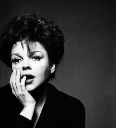 a black and white photo of a woman with her hand on her chin, looking at the camera