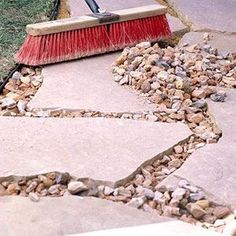 a red broom sitting on top of a sidewalk next to a pile of rocks and grass