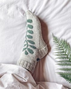 a pair of socks sitting on top of a bed next to a green fern leaf