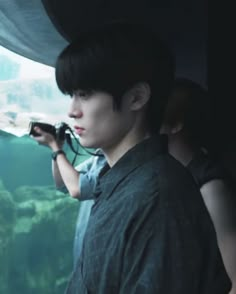 a young man holding a camera looking out the window at some fish in an aquarium