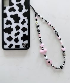 a black and white cow print phone case next to a pink beaded lanyard