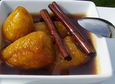 a white bowl filled with apples and cinnamon sticks next to a spoon on top of a table