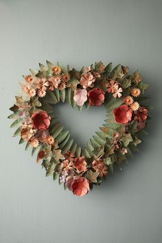 a heart shaped wreath hanging on the wall with flowers and leaves around it in front of a gray wall