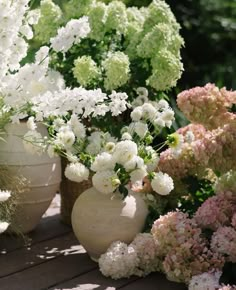 several vases filled with white and pink flowers on a wooden table in the sun