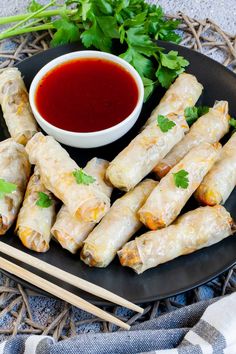 a black plate topped with spring rolls and dipping sauce