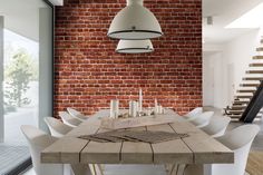 a dining room table with white chairs next to a brick wall and stairs in the background