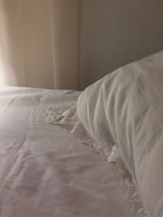 an unmade bed with white linens and lace on the pillowcase, in front of a window