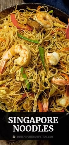 a pan filled with noodles and shrimp on top of a wooden table