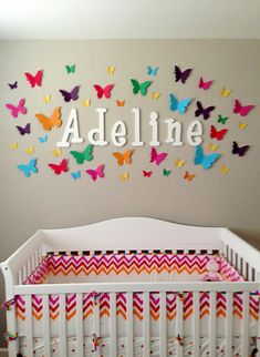 a white crib in front of a wall with colorful butterflies and name on it