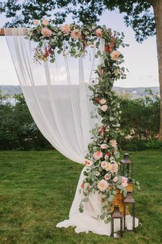 a wedding arch with flowers and greenery on the grass near a bench in front of a tree