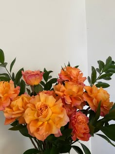 a vase filled with lots of orange flowers on top of a wooden table next to a white wall