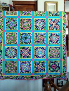 a blue and green quilt hanging on a wall