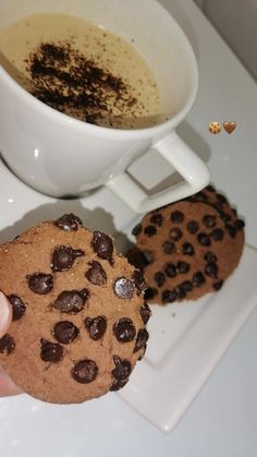 a person holding a chocolate chip cookie next to a cup of coffee