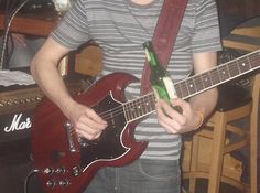 a young man holding a red guitar in his right hand and wearing a striped shirt