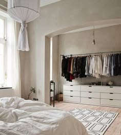 an unmade bed sitting in a bedroom next to a white dresser and closet filled with clothes